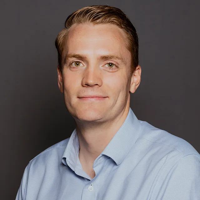 A portrait of Daniel Scott, a man with short blond-red hair and a blue shirt.