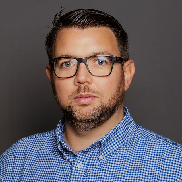 Portrait of Neil Gray, a man with short black hair and a white and blue checked shirt.